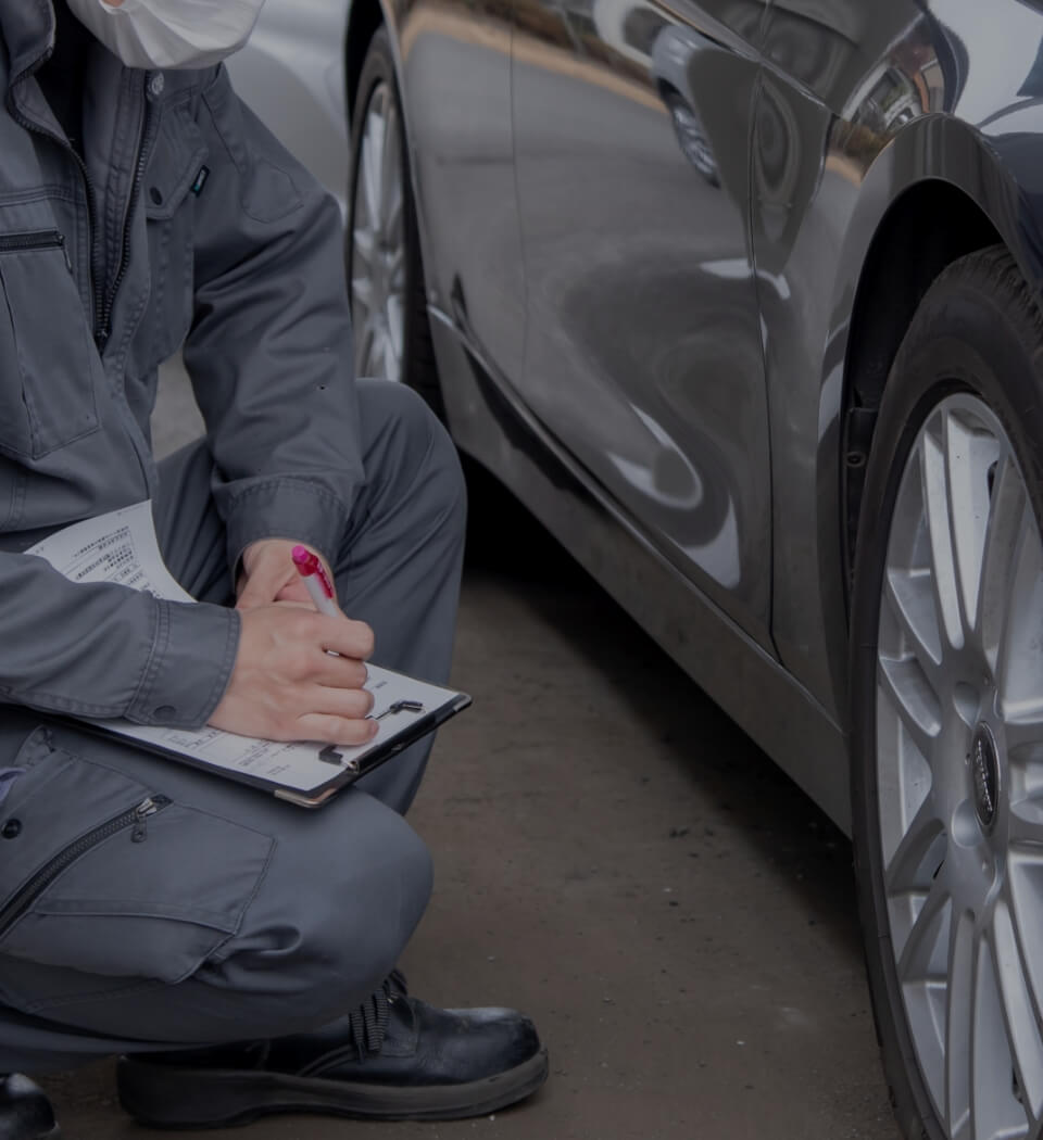 自動車の横でバインダーを持った人がしゃがんでいる写真